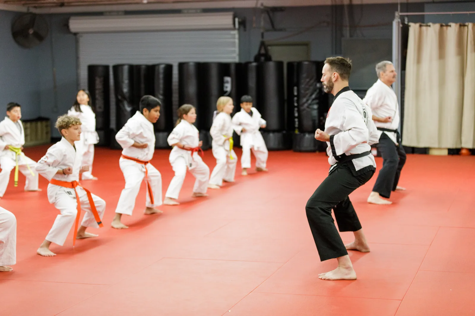 Children in uniform sit on the mat while an instructor leads an after-school martial arts class at Santa Barbara Dojo