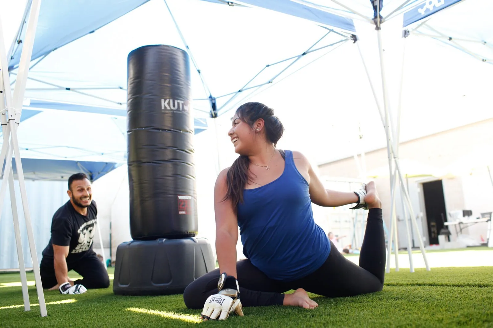A student stretching beside a heavy bag while an instructor coaches during outdoor training