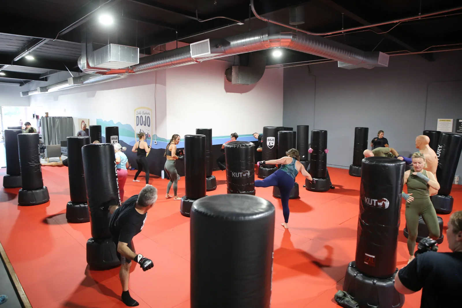 A coach guides a beginner through a heavy-bag combination in a first kickboxing class at Santa Barbara Dojo