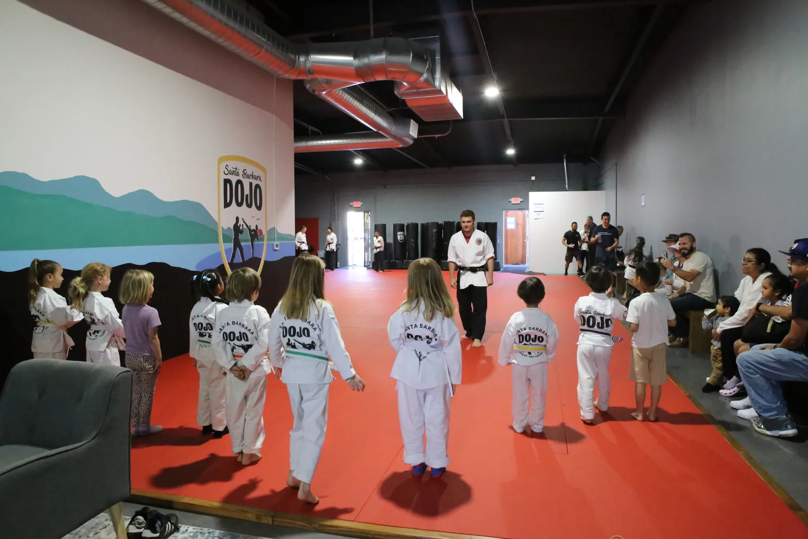 A child practices a front kick while parents watch from the side of the mat at Santa Barbara Dojo
