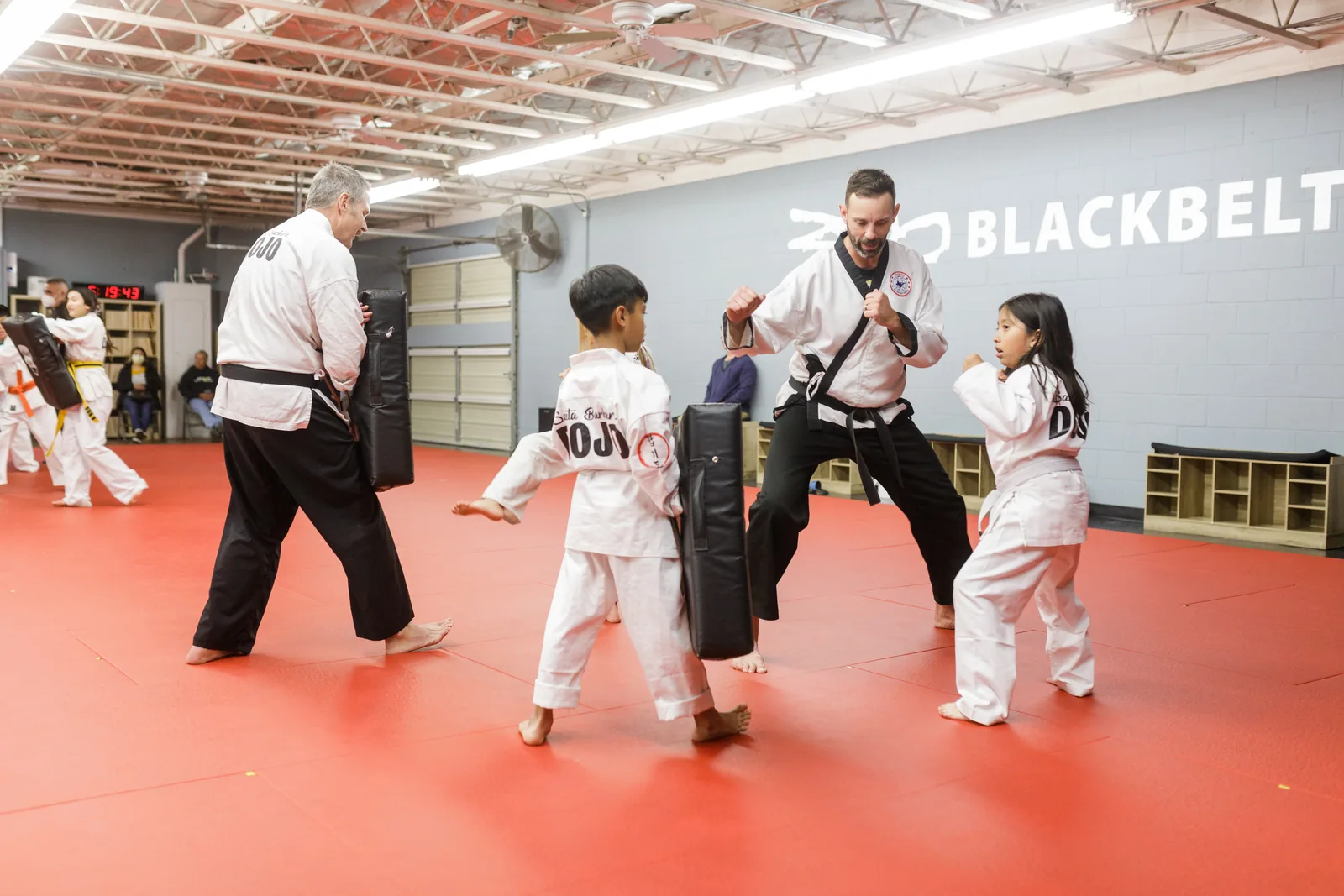 A child holds a focus mitt while an instructor demonstrates a self-defense strike at Santa Barbara Dojo