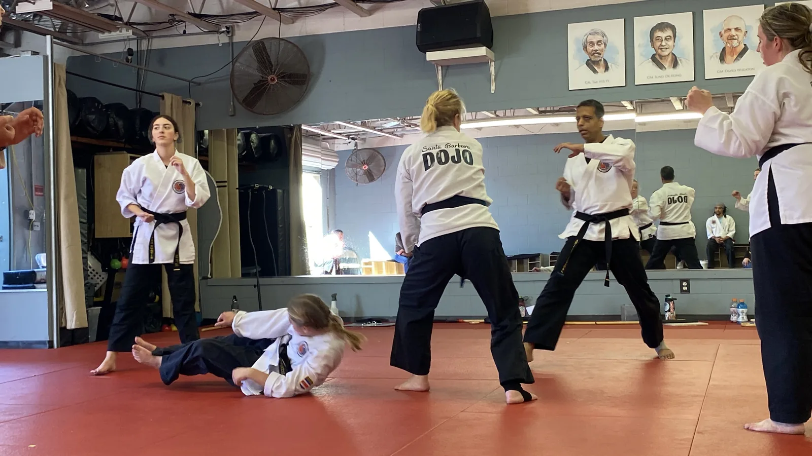 A student throws a partner to the mat during the self-defense seminar as black belts look on